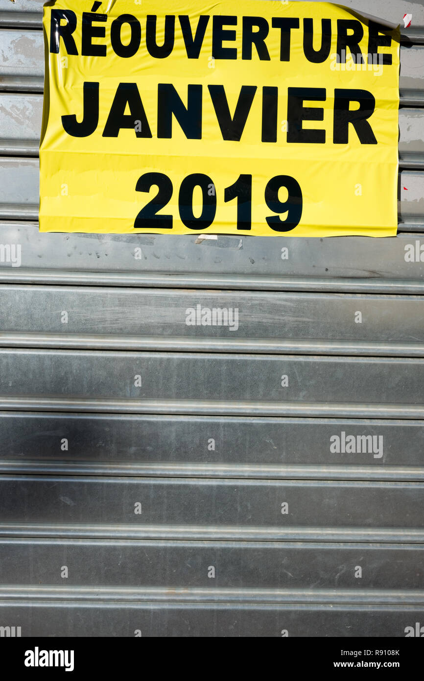 cropped view of crumpled yellow sticker on closed metal shop blind with a phrase in french saying, Reopening January 2019, Montpellier, France Stock Photo