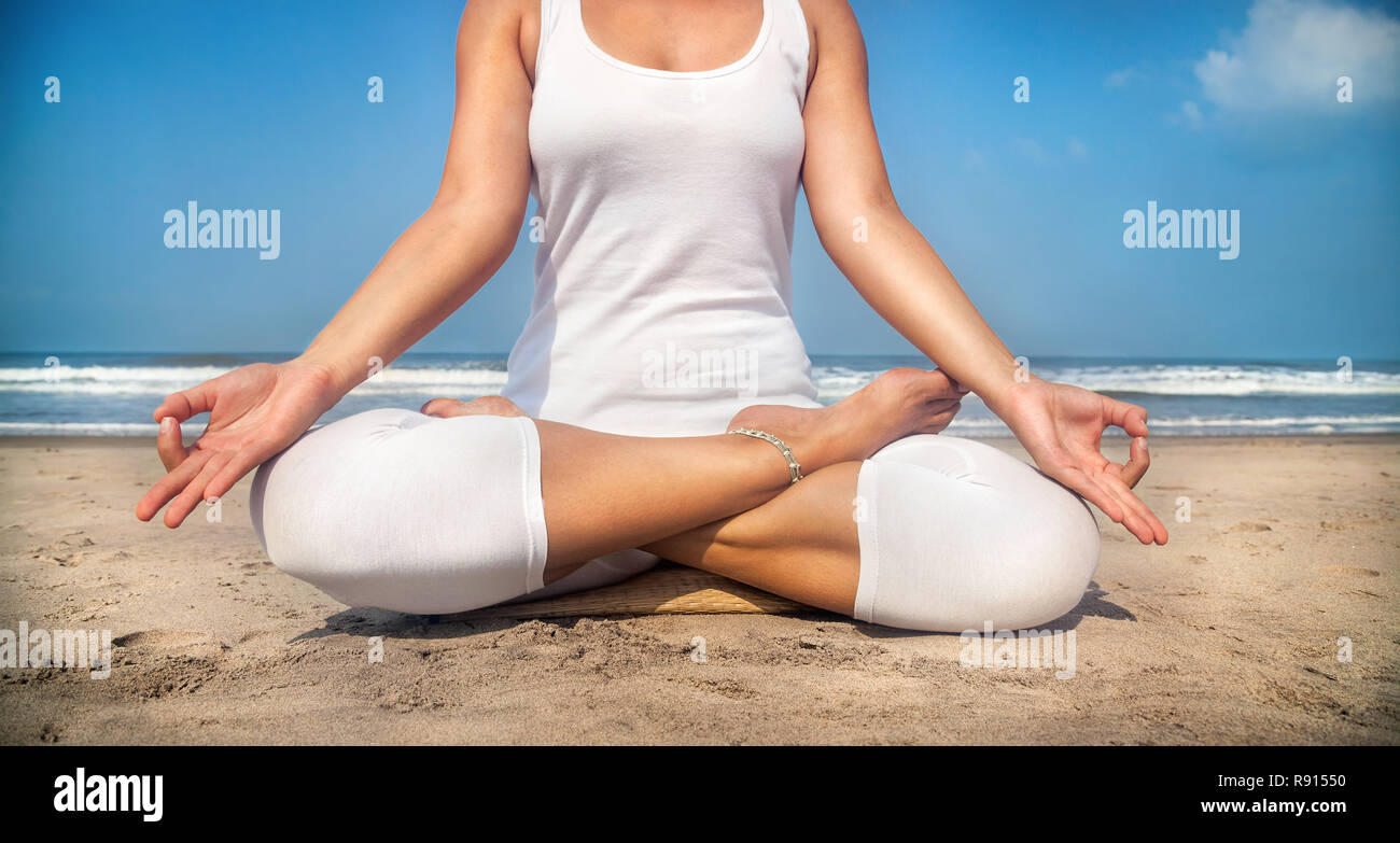 Woman doing yoga meditation in white costume on the beach in Goa, India Stock Photo