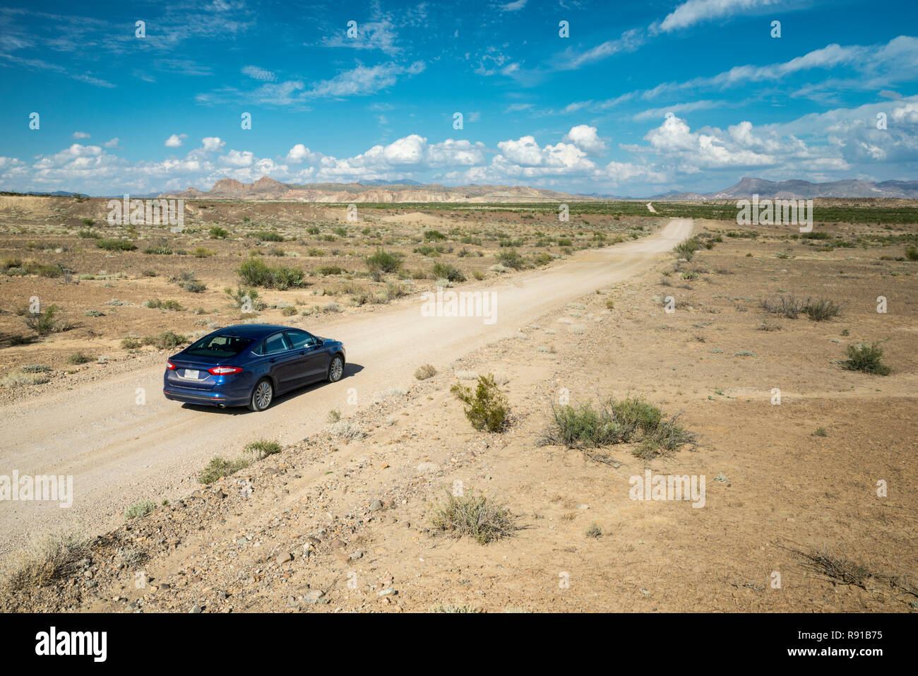 Blue sedan car on a road trip in the USA. Arid climate on a sunny day. Stock Photo