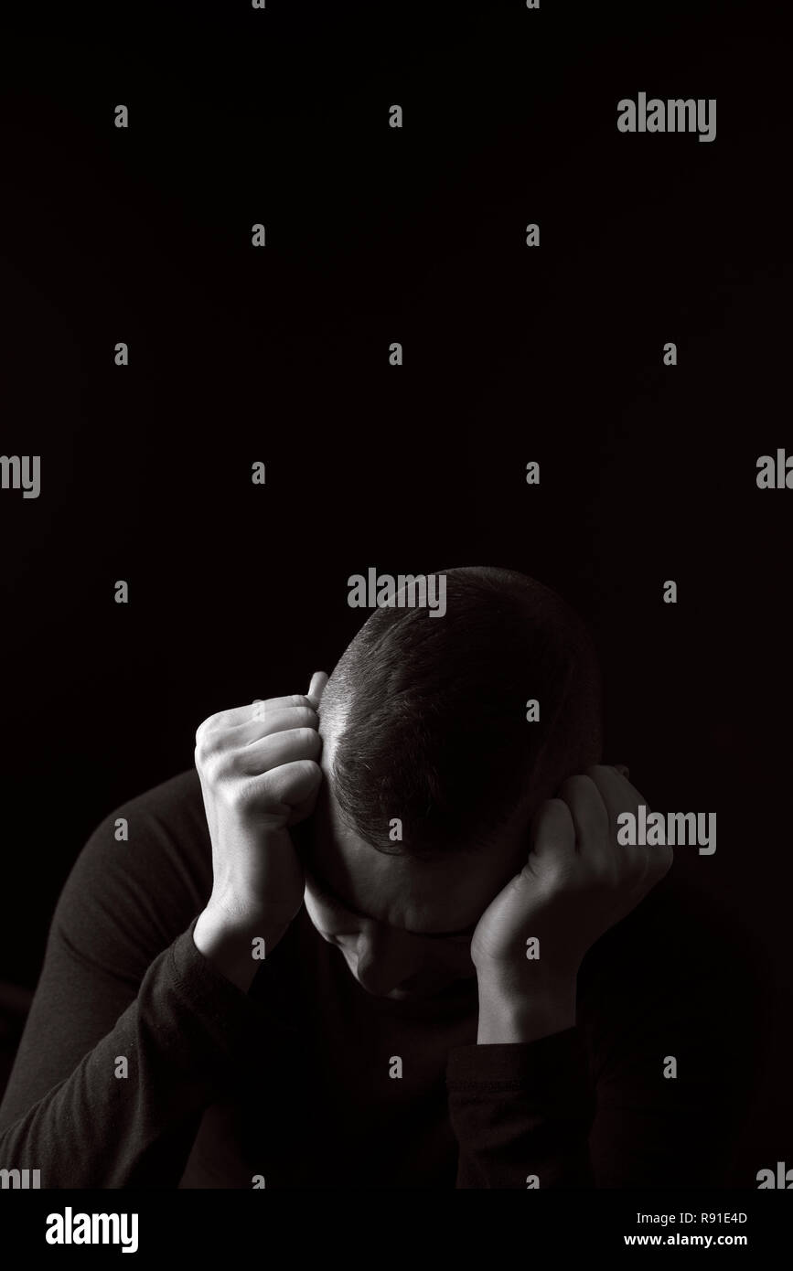 closeup of a desperate young caucasian man with his hands in his head, against a black background, with some blank copy space around him, in black and Stock Photo