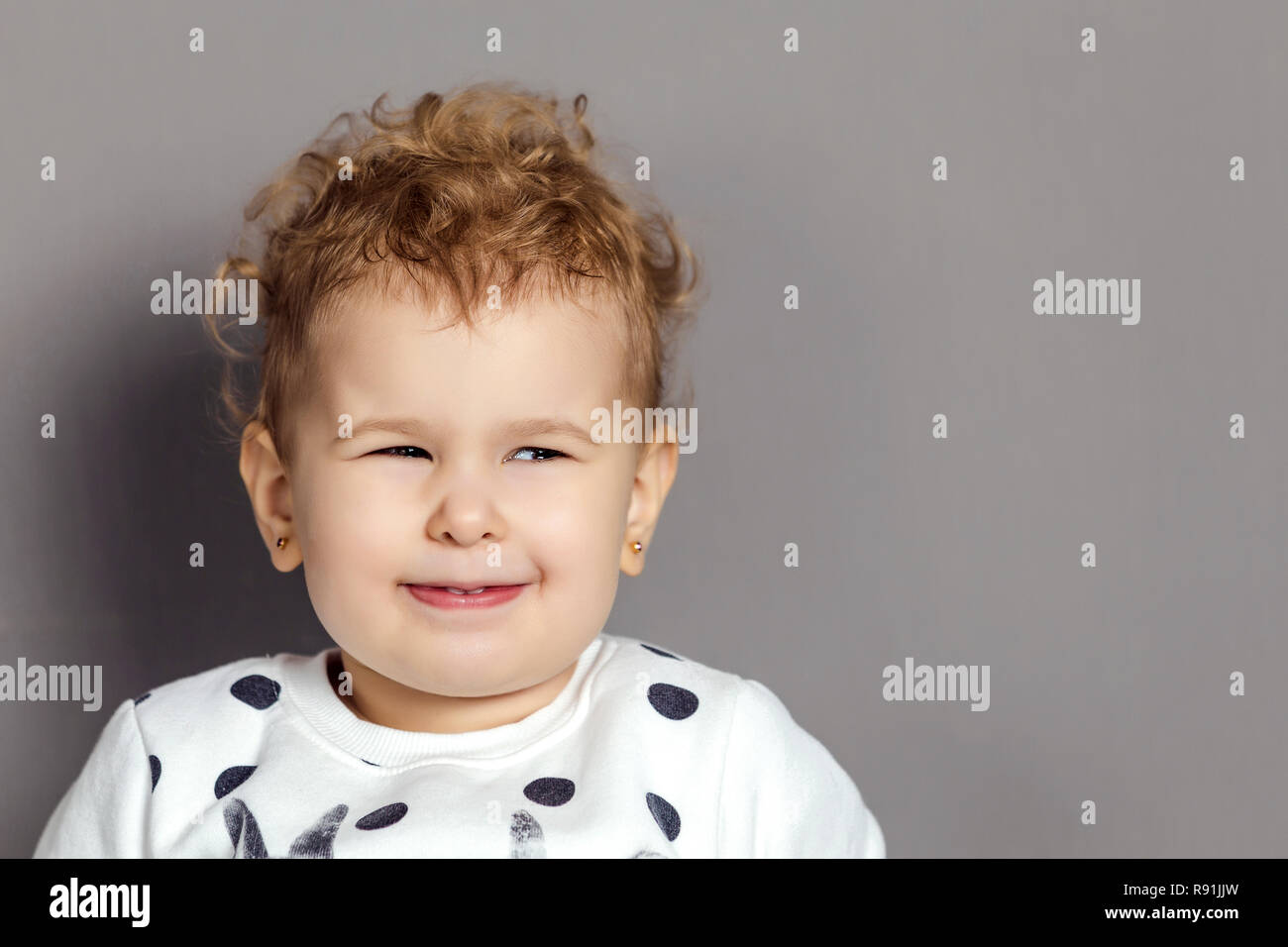 little curly-haired blonde girl with a sly facial expression looks to the side Stock Photo
