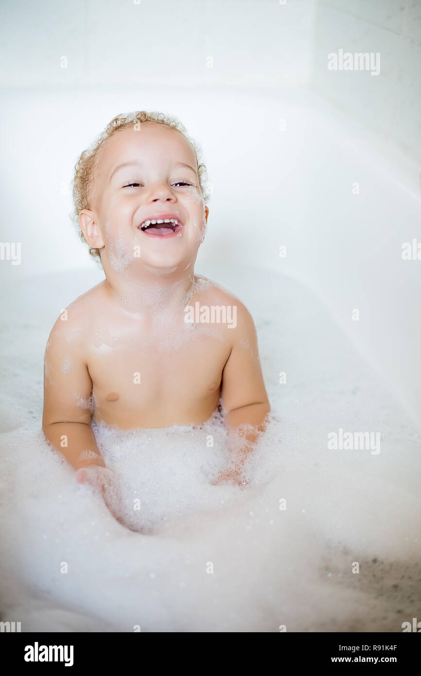 Closeup two year old child having fun with foam by bathing in bathtub