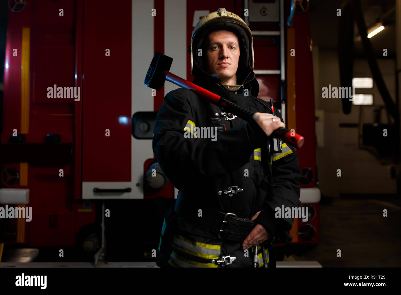 Photo of fireman in protective helmet with hammer on background of fire