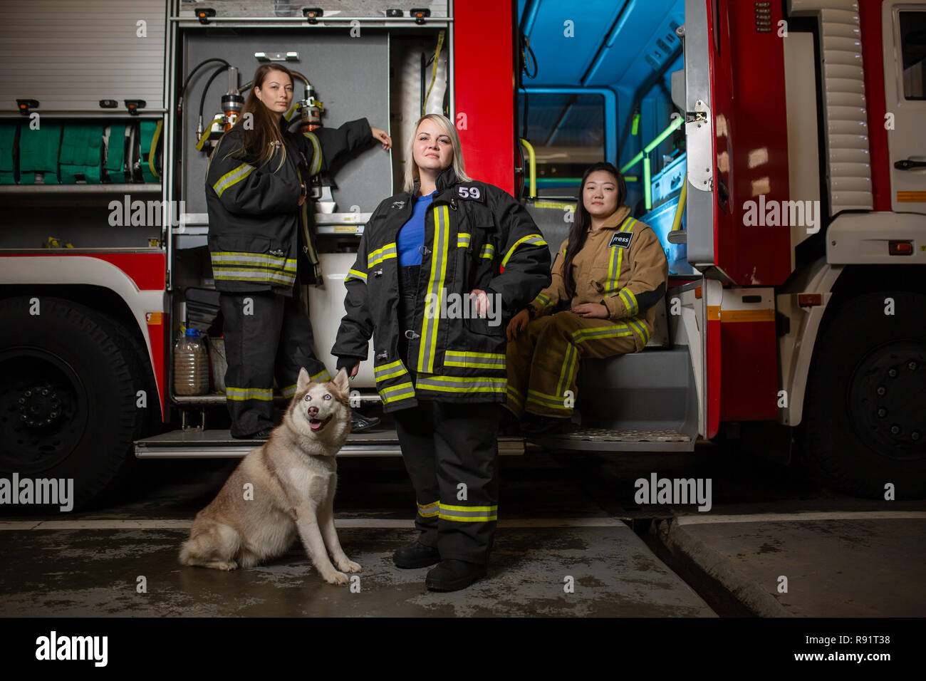 Photo of three women firefighters and dog on background of fire truck Stock Photo