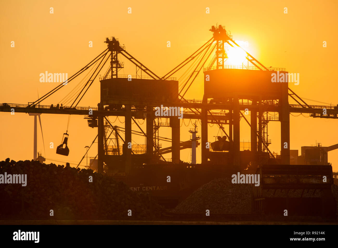 Silhouetted cranes unloading coal at sunset by the Tata steel works in Ijmuiden, North Holland, Netherlands Stock Photo