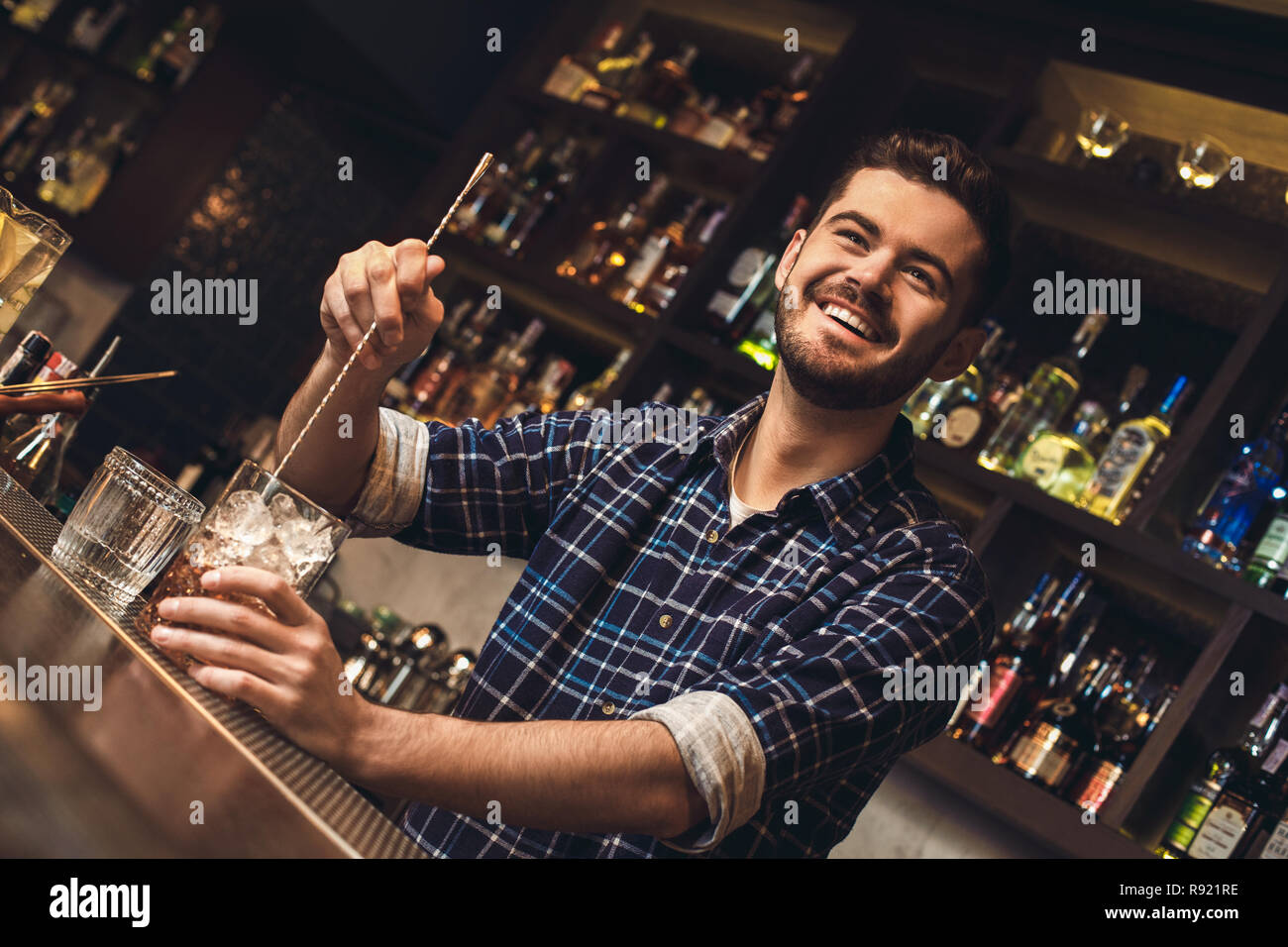 Young barman standing at bar counter mixing alcohol with ice looking ...