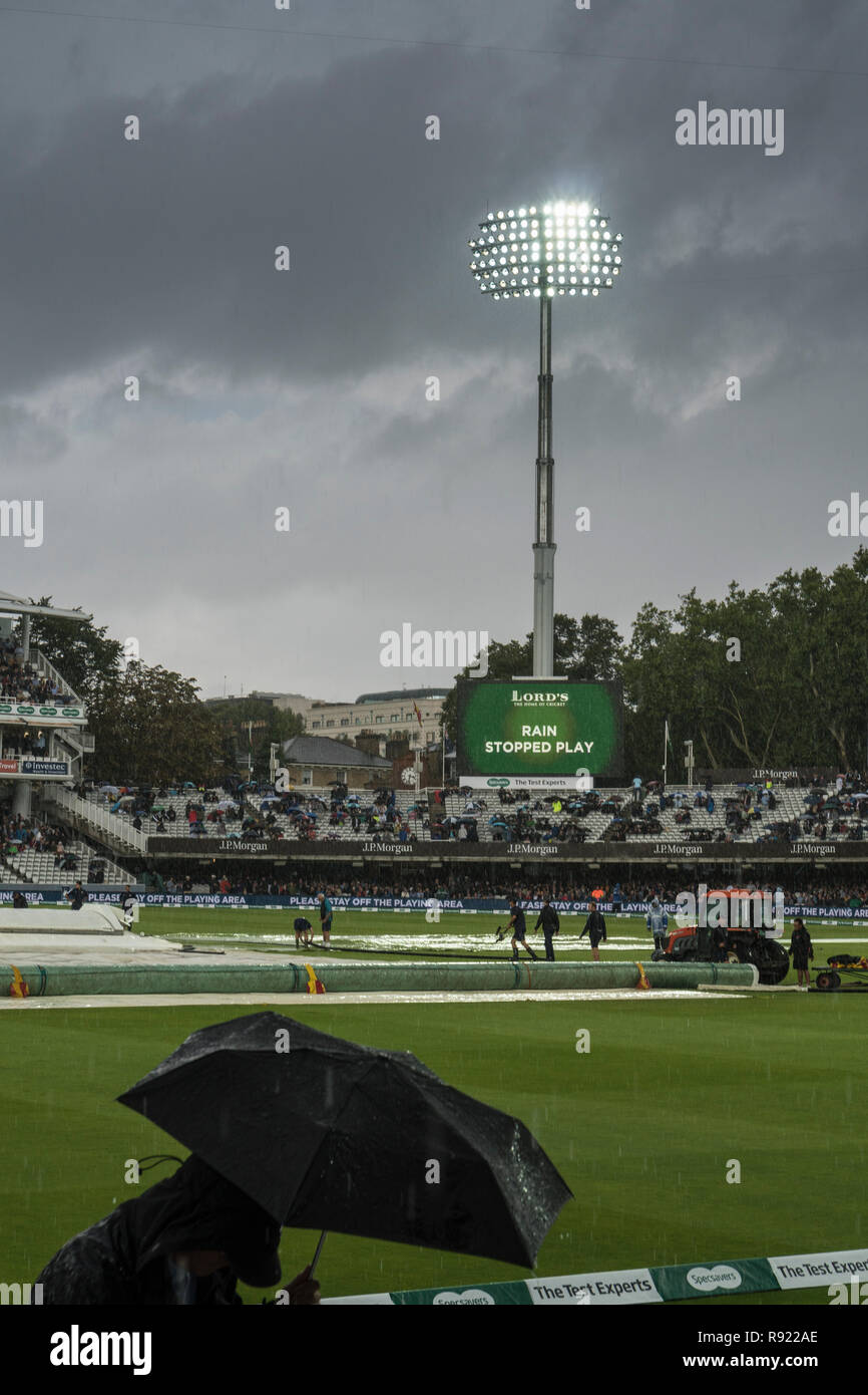 Heavy rain during a test match at Lords. The floodlights blaze brightly against an angry grey sky. In the foreground a spectator runs for cover Stock Photo