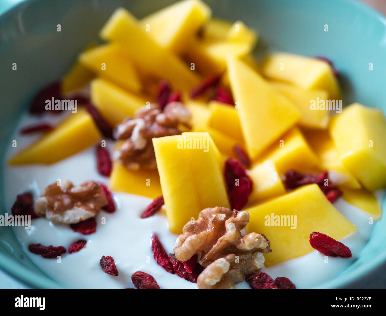 Delicious fruit bowl with mango, raspberry, goji berries and walnuts on red background Stock Photo