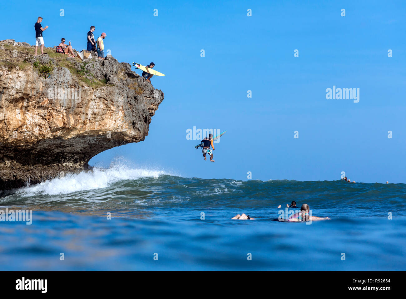 Surfers jumping form cliff into sea, Jimbaran, Bali, Indonesia Stock Photo