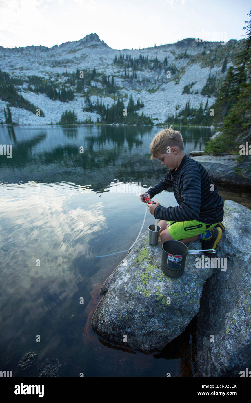 Side view shot of a boy filling a water bottle from a lake, Selkirk Mountains, Sandpoint, Idaho, USA Stock Photo