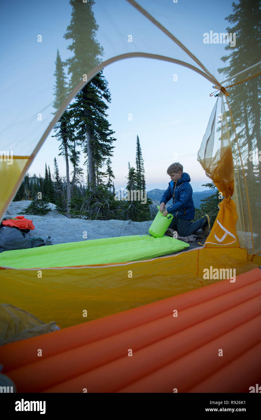 Photograph of a 10 year old boy near a tent preparing for camping, Selkirk Mountains, Sandpoint, Idaho, USA Stock Photo