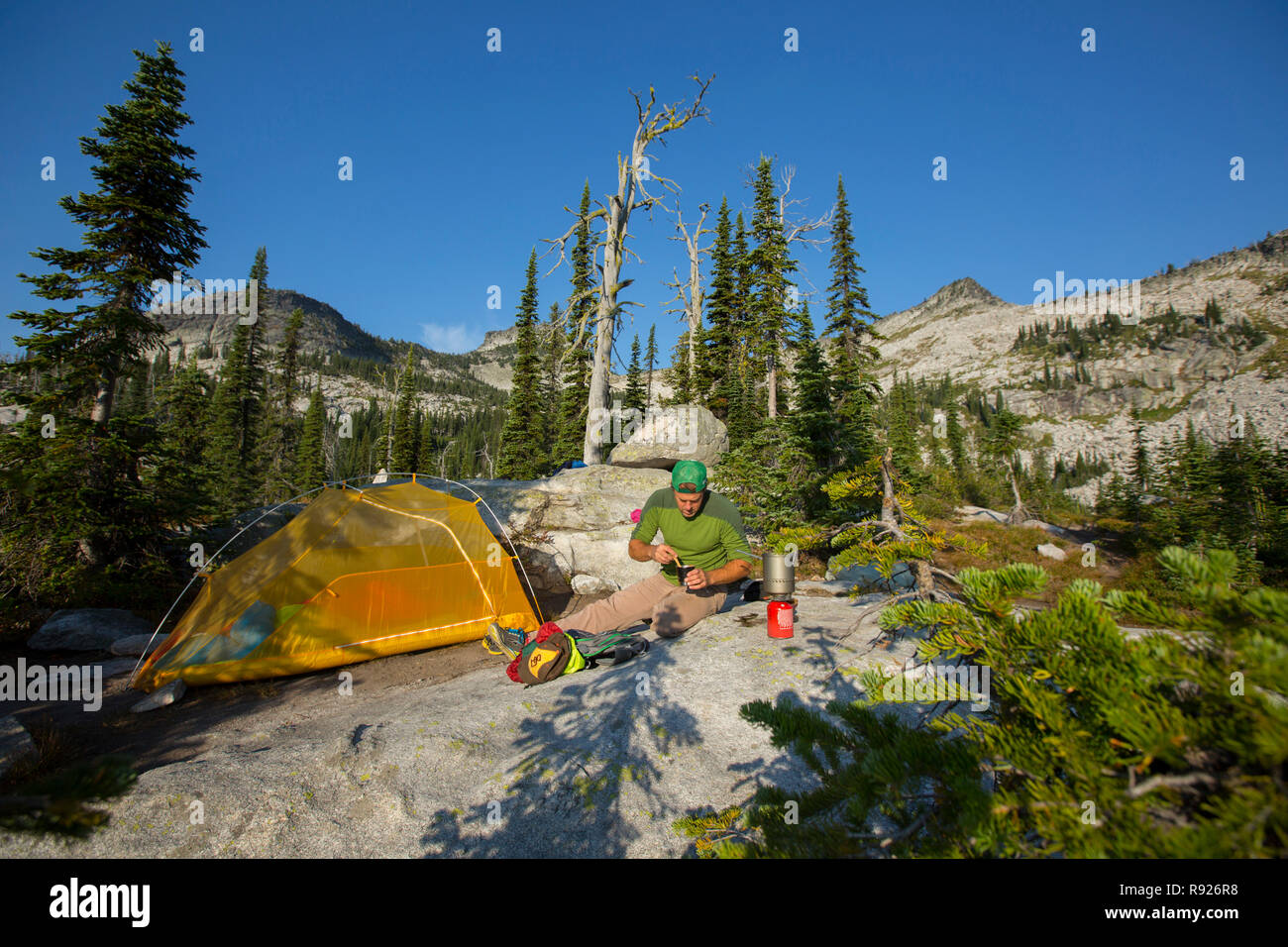 Distant view of a man making coffee near a camping tent, Selkirk Mountains, Sandpoint, Idaho, USA Stock Photo