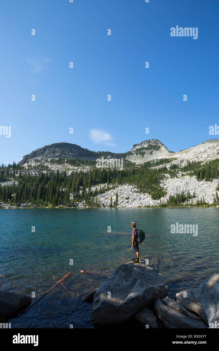 Photograph of a young backpacker on the shore of Beehive Lake while on a hiking trip, Selkirk Mountains, Sandpoint, Idaho, USA Stock Photo