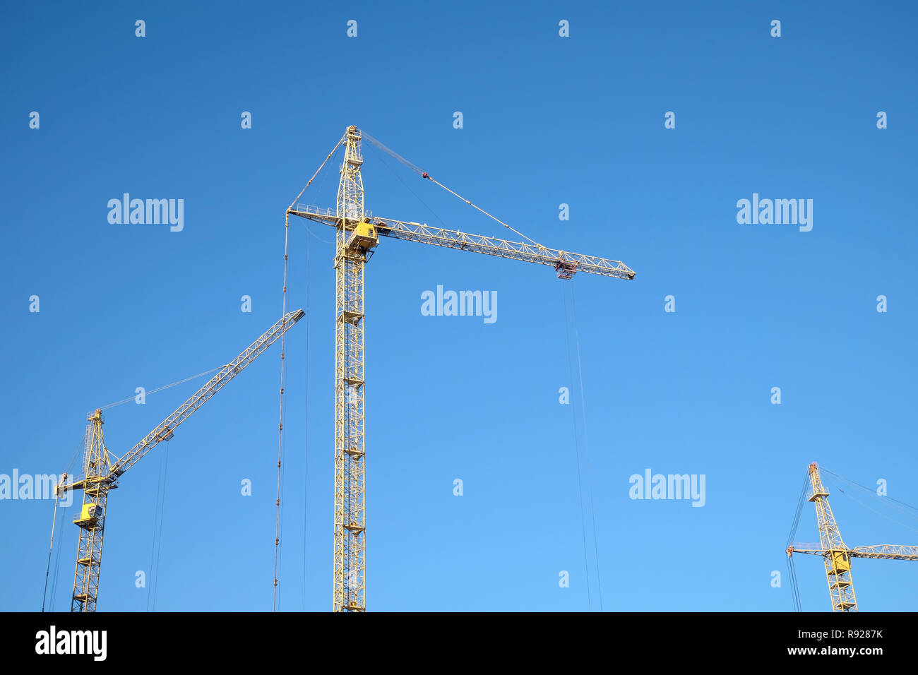 Big yellow construction tower crane over clear blue sky as background