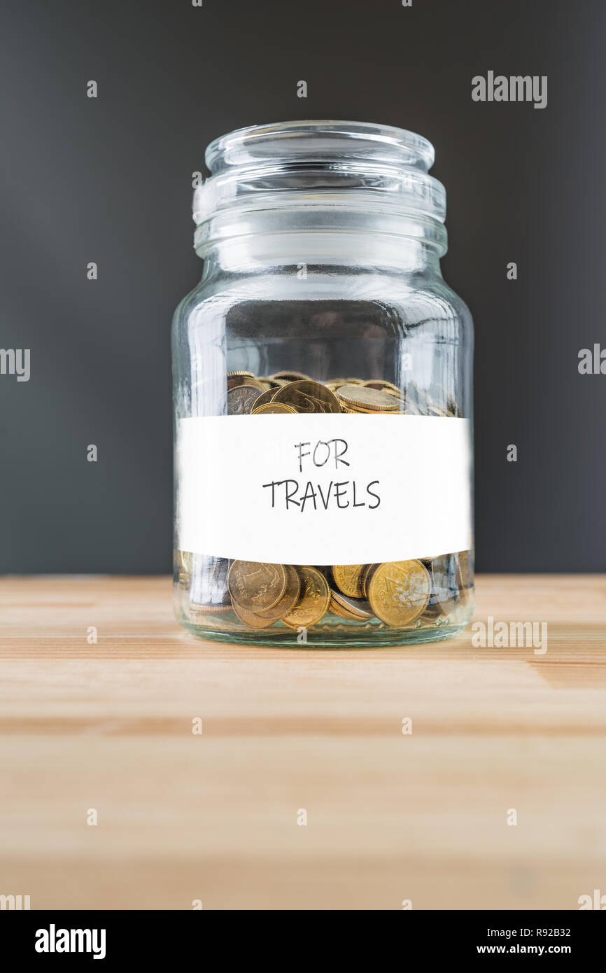 Jar with golden coins on natural wooden background. Money saving for travels abstract concept. Stock Photo