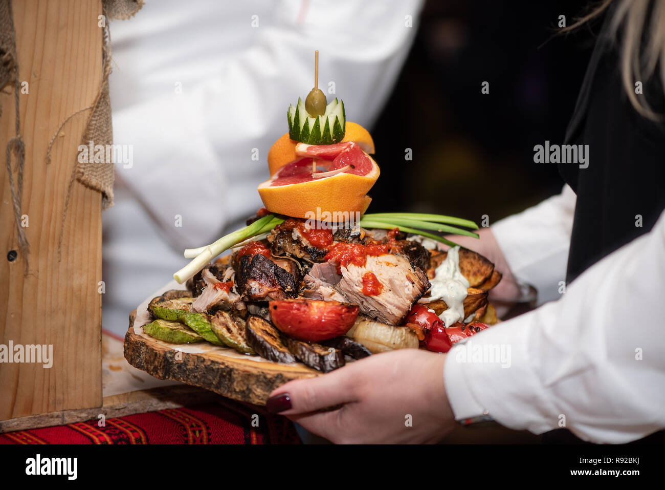 Baked potatoes with vegetables and fruits on wooden stand, delicious dish in restaurant. Stock Photo