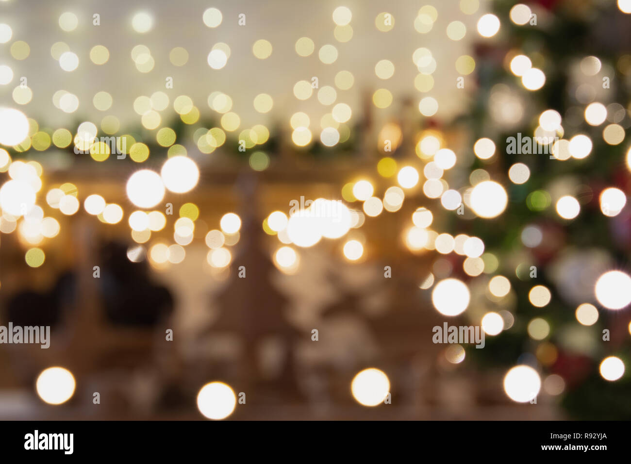 Abstract composition. Beautiful blurred Christmas interior with fireplace, wood mantelpiece, lit up Christmas tree, warm yellow and colorful lights, candles, toned Stock Photo