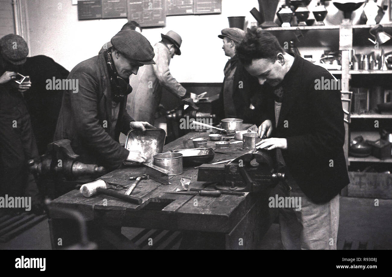 1940s, historical, former mine workers, most wearing coats and cloth caps in a workshop doing metal work making metal trays. As the mines closed efforts were made to retrain the former workers, so they could learn new skills. Stock Photo