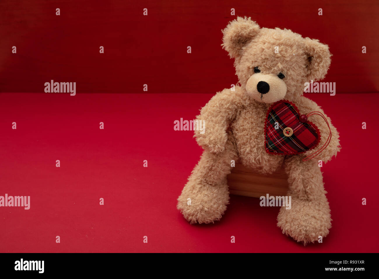 Valentines day. Top view of isolated teddy bear with a fabric heart against red background, copy space Stock Photo