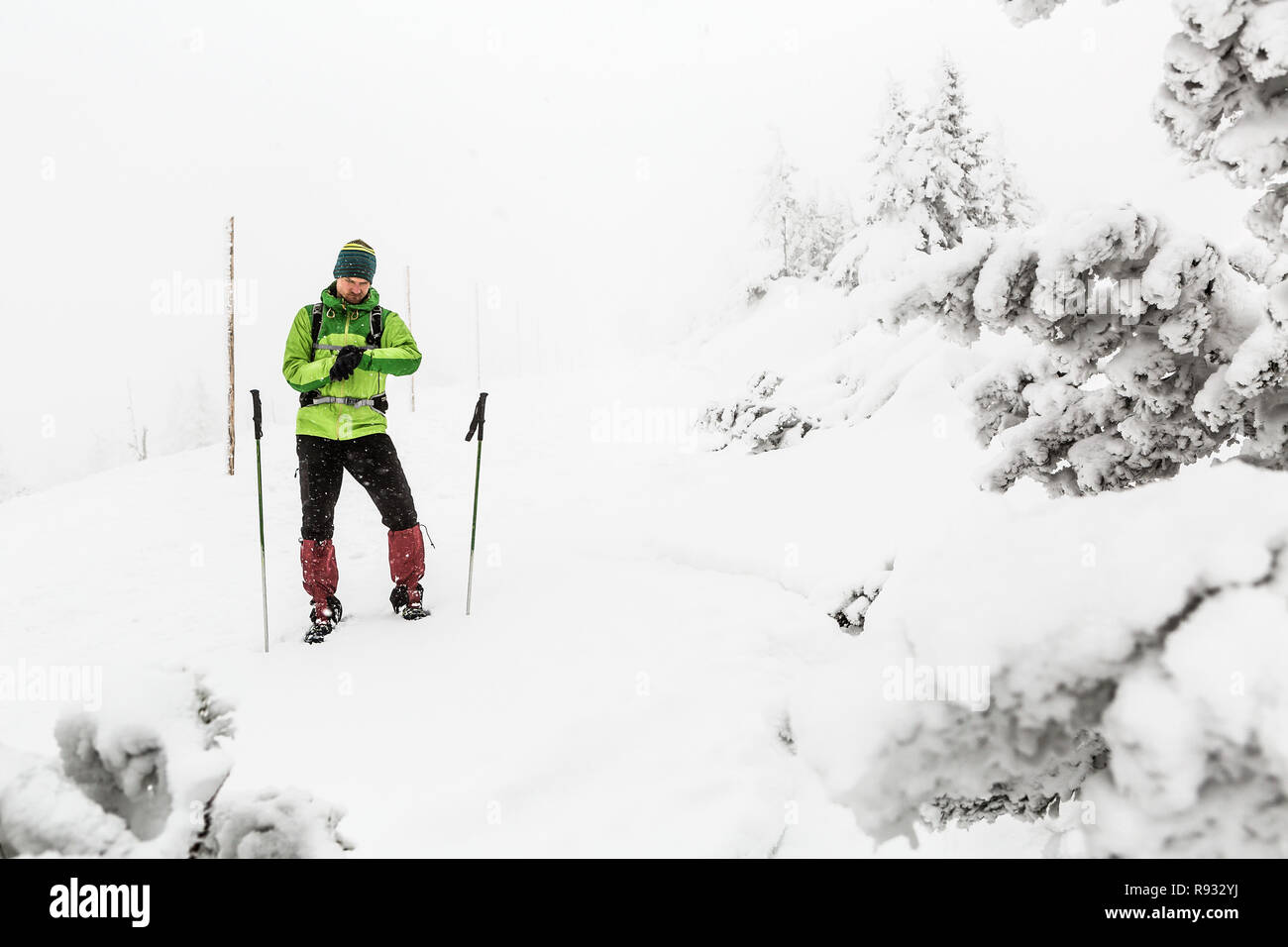 Man lost on winter trekking expedition in white snowy mountains with snow blizzard. Using GPS smart watch to find a way, adventure and expedition conc Stock Photo