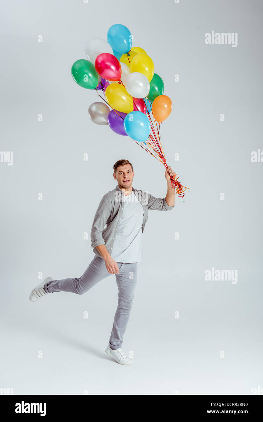 man jumping with bundle of colorful balloons and looking at camera on grey background Stock Photo