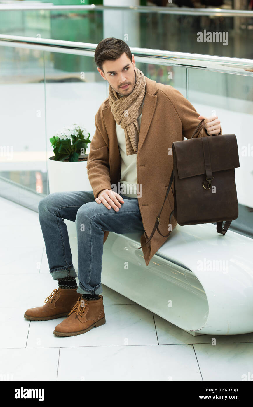 Handsome Man Holding Bag And Sitting On Bench In Shopping Mall