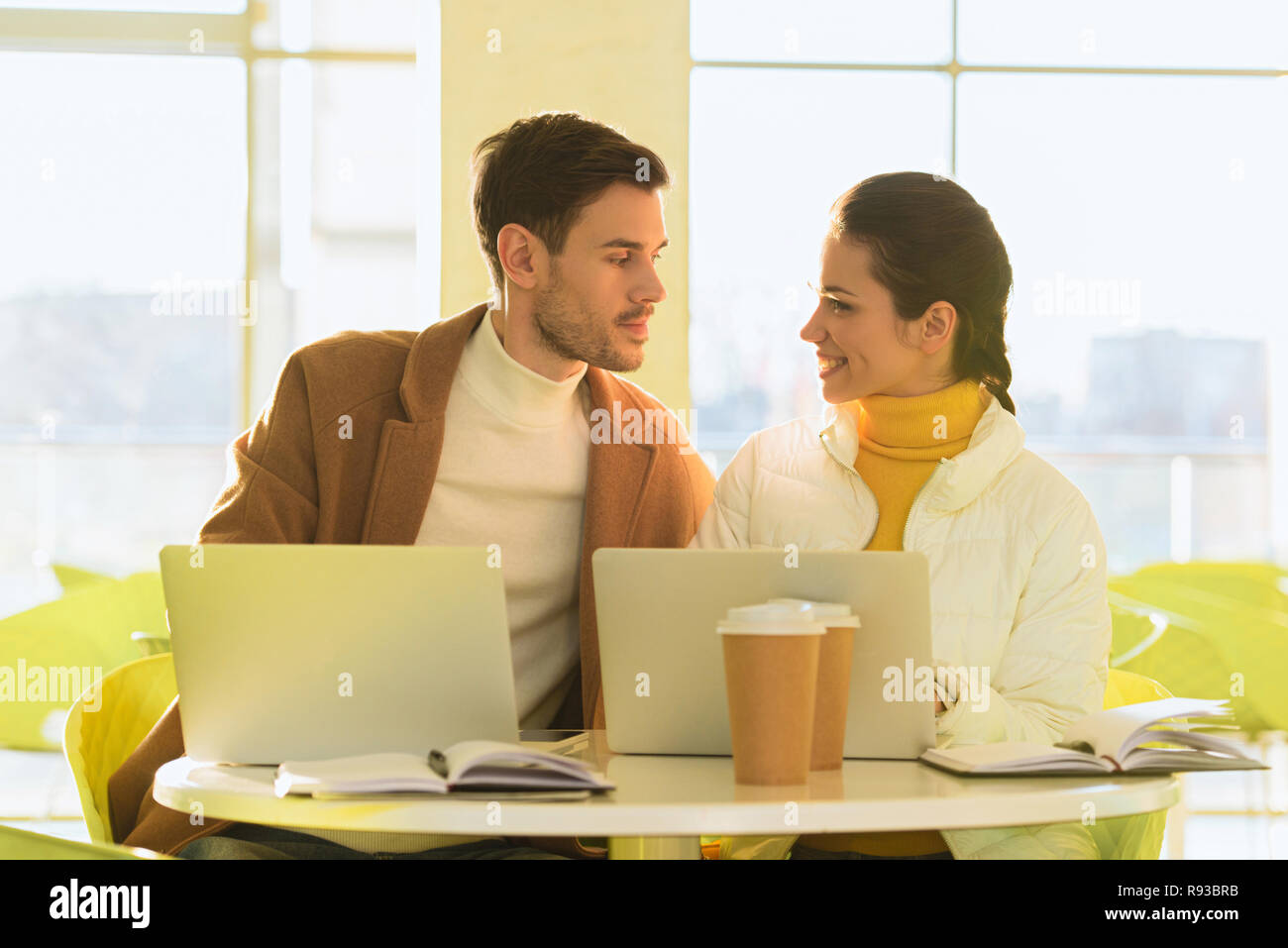 loving couple sitting at table with laptops and looking at each other in cafe Stock Photo