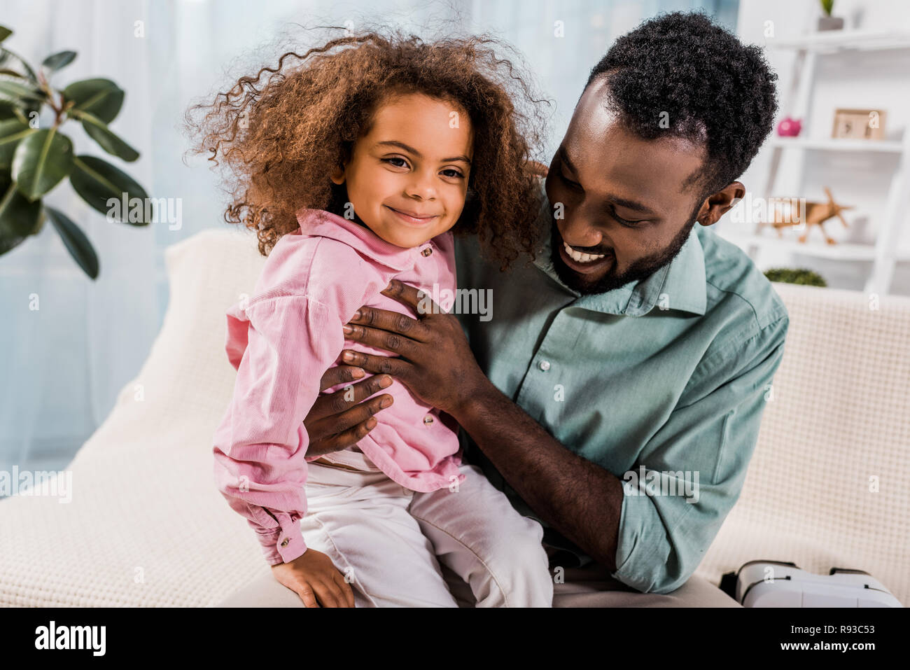 african american dad holding smiling daughter on knees in living room ...