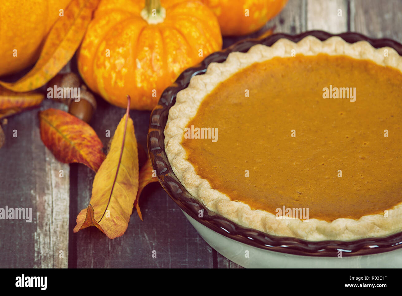 Pumpkin pie with pumpkins, golden autumn leaves, and acorns, on rustic table. Stock Photo
