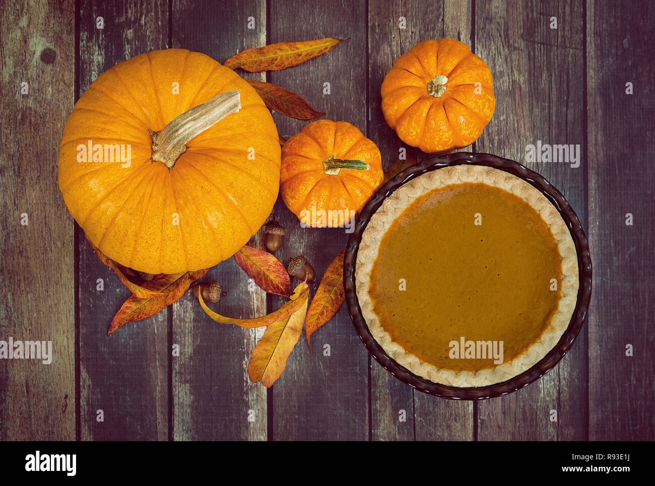 Pumpkin pie displayed with pumpkins, golden autumn leaves, and acorns on rustic wooden table. Top view. Stock Photo