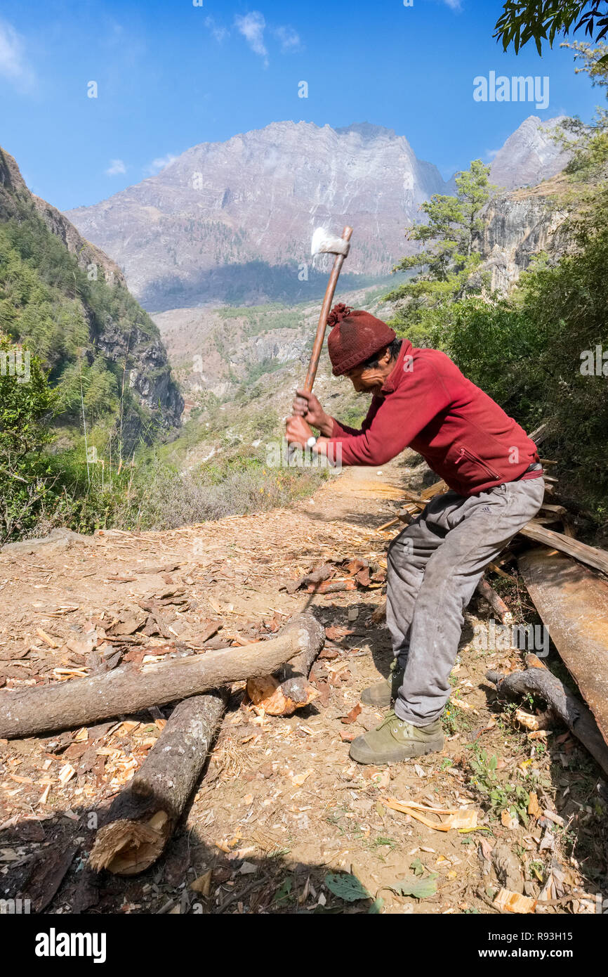 Nepalese man chopping wood in a Himalayan valley Stock Photo