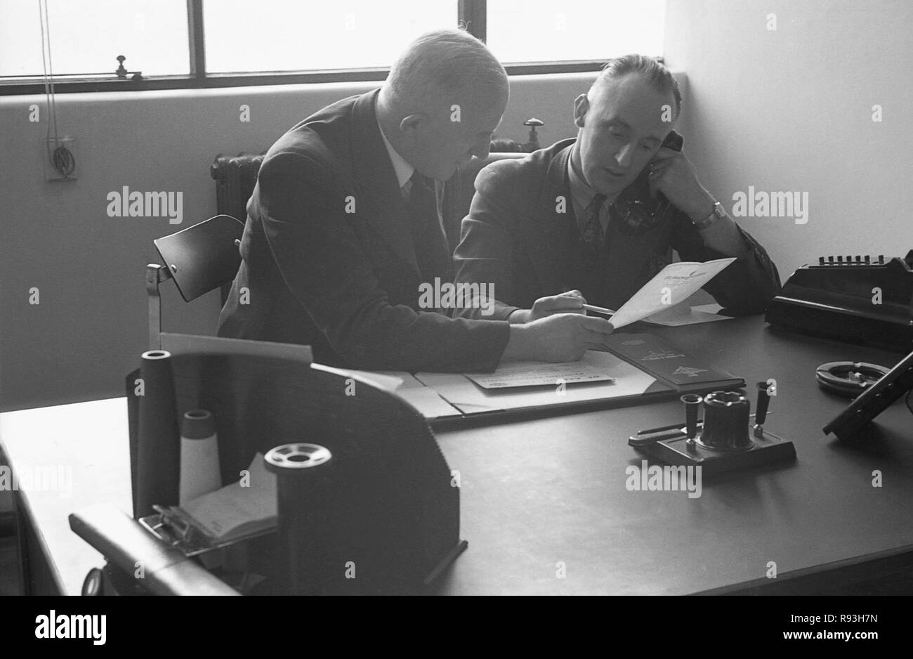 1940s, two company Directors of a synthetic silk factory sitting in an office, both behind a desk, one holding a letter and the other speaking on the telephone about its contents, South  Wales, UK. Stock Photo