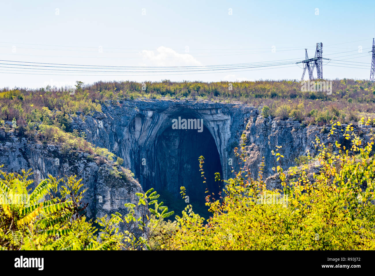 The huge entrance of the Prohodna cave in Northern Bulgaria, electric poles and wires on top, an example of juxtaposition Stock Photo