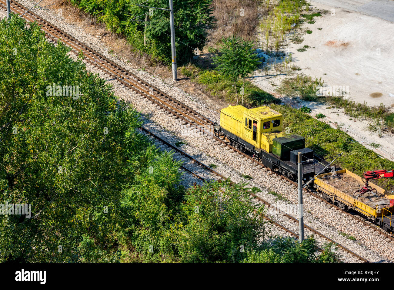 Yellow railway service diesel engine moving on rail line dragging wagons with pebbles and small red crane going to construction site. Rural Bulgarian  Stock Photo