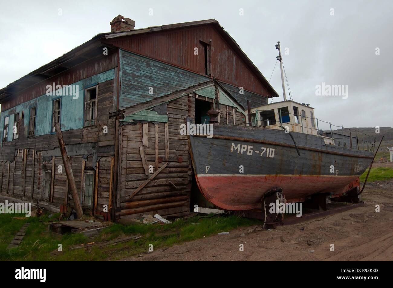 Derelict small fishing boat, MRB, in front of a derelict house in a rural locality, Dalniye Zelentsy, Kola Peninsula Stock Photo