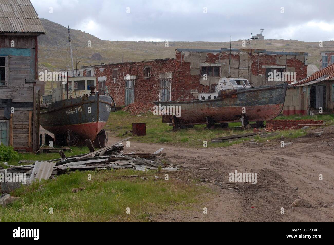 Derelict small fishing boats, MRB, in front of derelict houses in a rural locality, Dalniye Zelentsy, Kola Peninsula Stock Photo