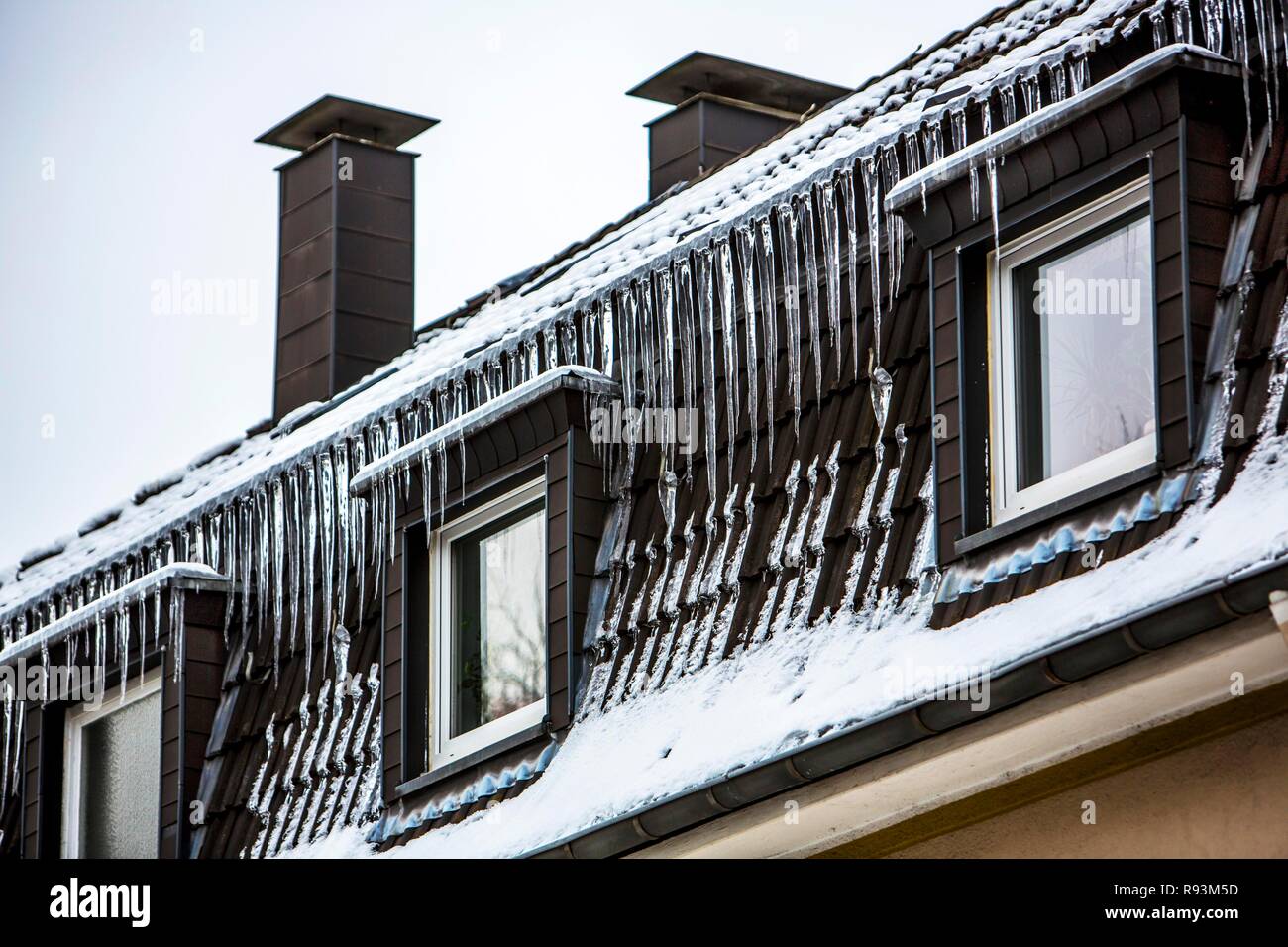 Large icicles hanging from the eaves of a house, sign of a poorly heat-insulated roof, Essen, North Rhine-Westphalia, Germany Stock Photo