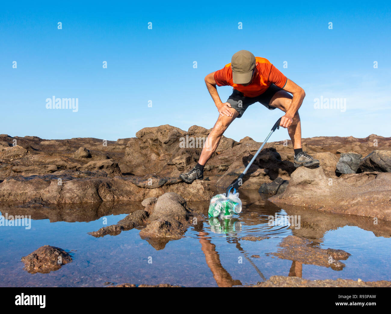 A Plogger/jogger collects plastic rubbish from beach during his morning run Stock Photo
