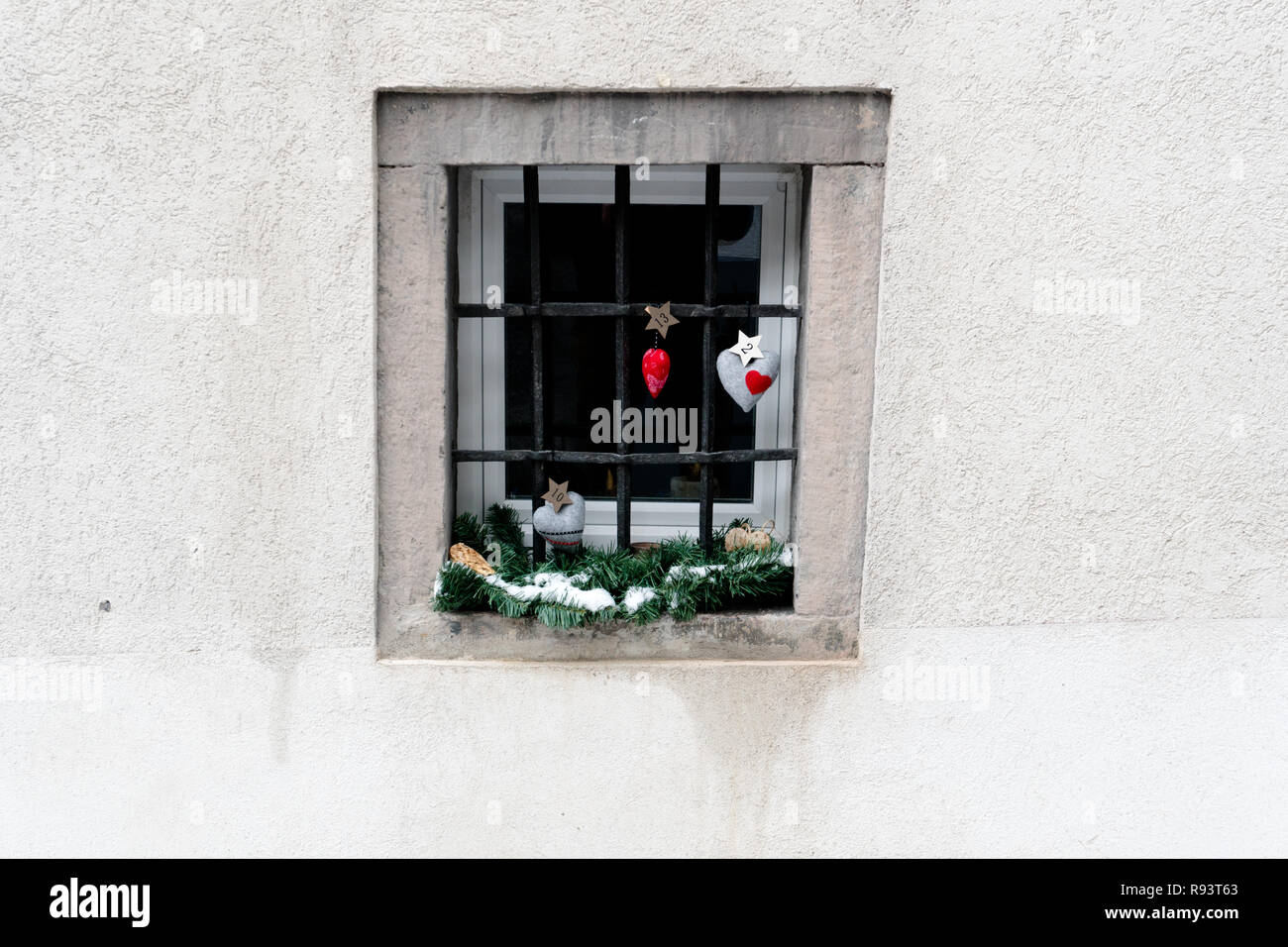 imaginative advent calendar and Christmas decorations hanging from a ground floor window in a snowy village in the Swiss Alps during the holidays Stock Photo
