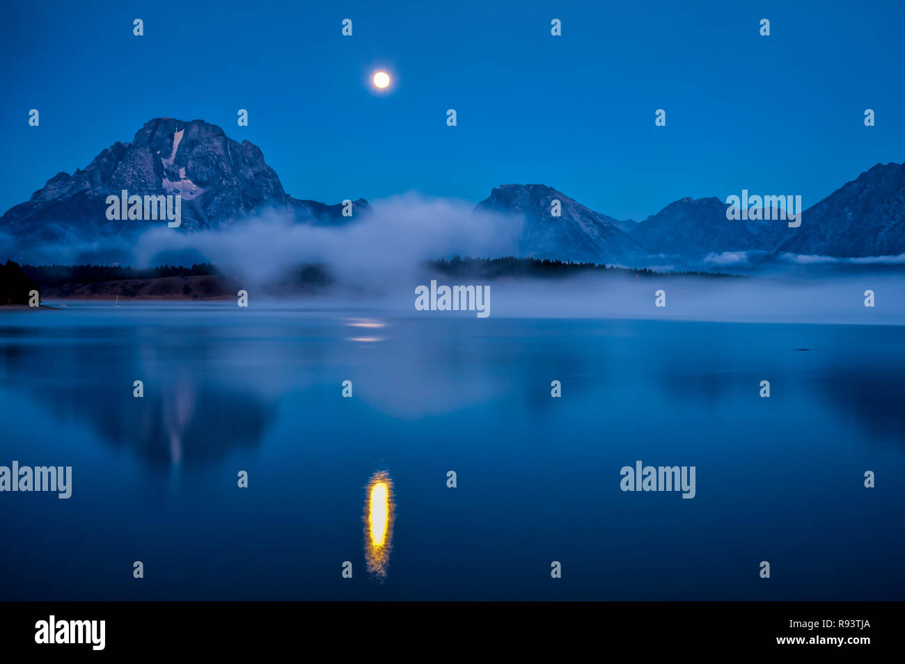 Moon Setting in the Early Morning over the Tetons and Jackson Lake Stock Photo