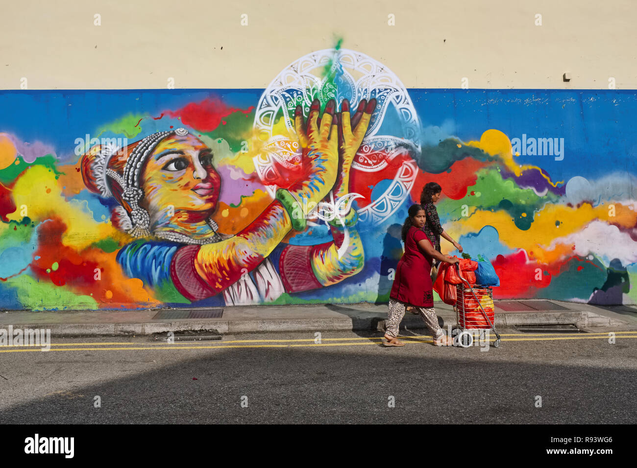Ethnic Indian pedestrians passing a wall painting depicting a classical Indian dancer, in Clive Street, Little India, Singapore Stock Photo