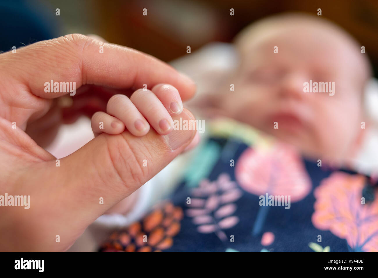Hand and fingers of a new born baby wrapped around an adult thumb. Stock Photo