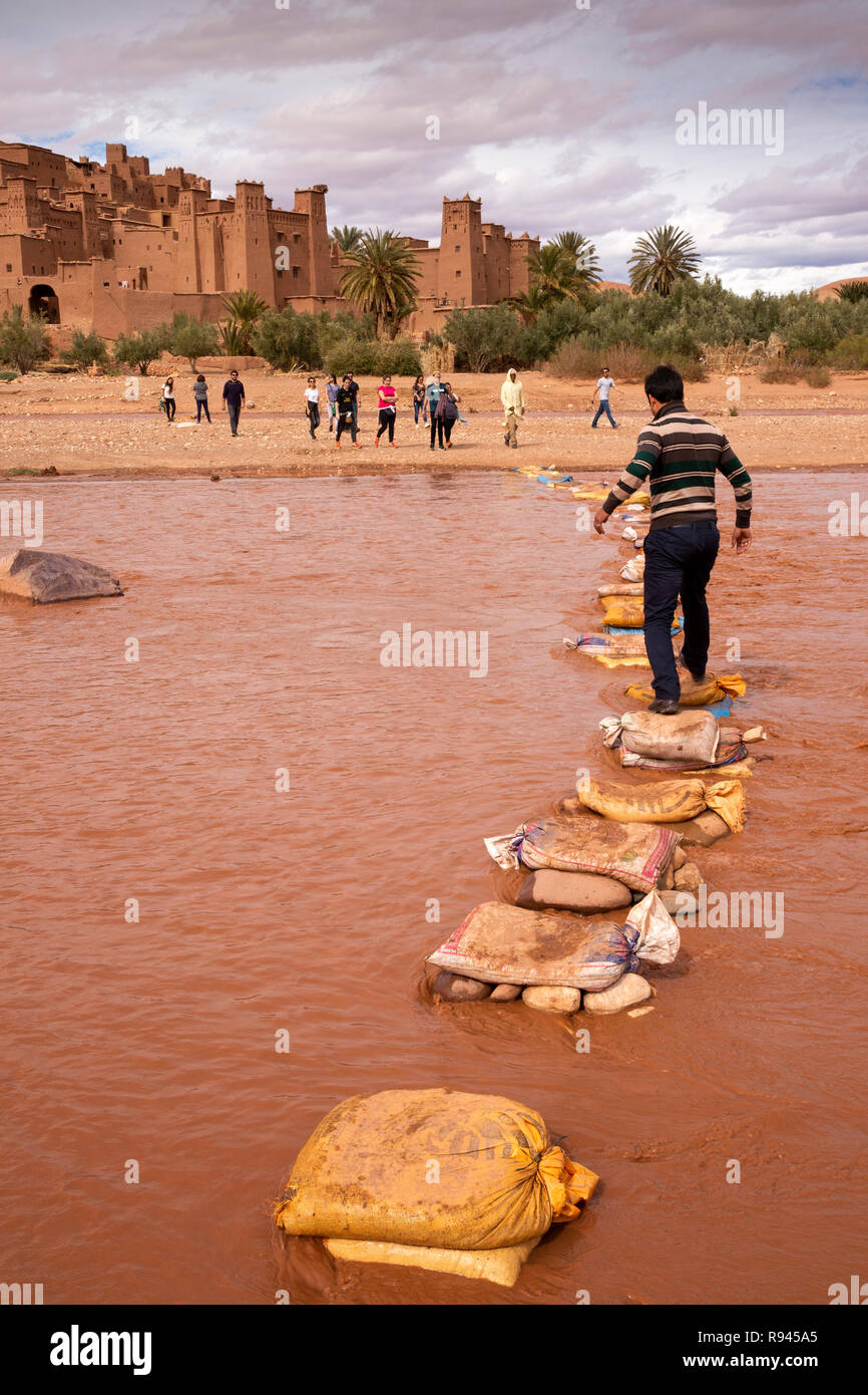 Morocco, Ouarzazate, Ksar of Ait-Ben-Haddou, Kasbah, man using Ounila River cement bag stepping stones Stock Photo