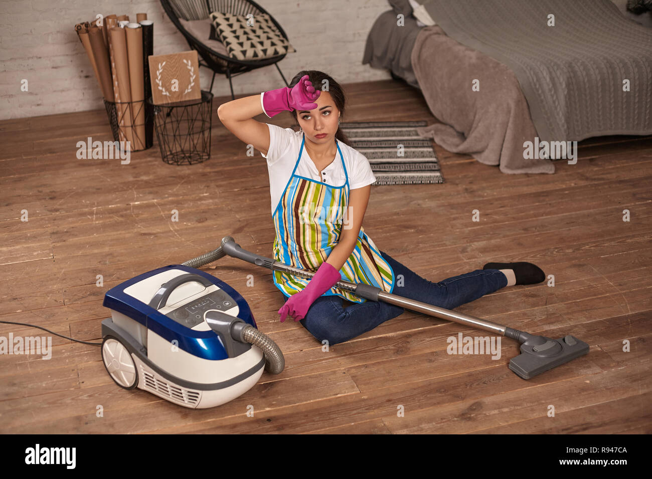 A young housewife sitting leaning on vacuum cleaner tired of housework ...