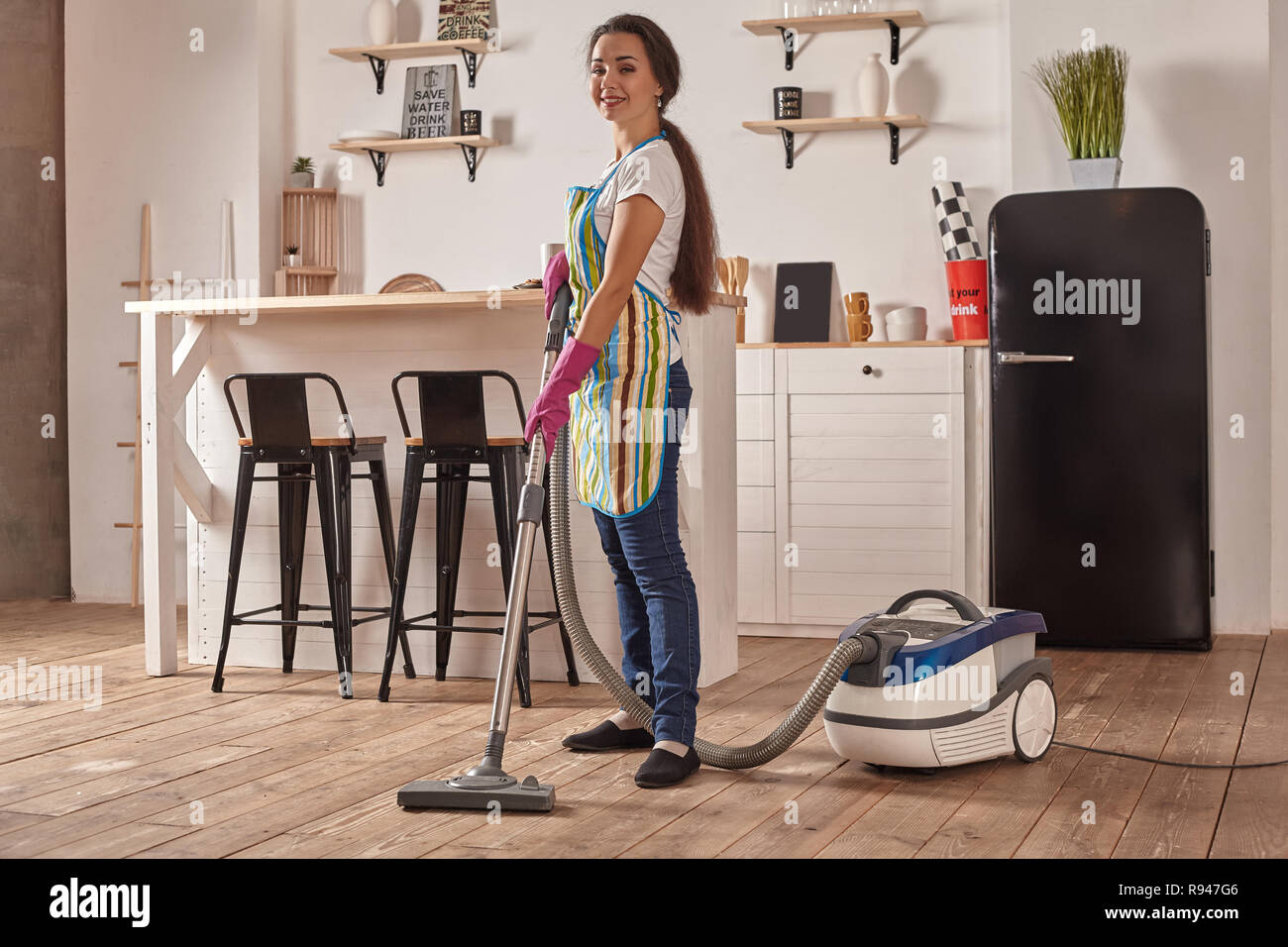Young woman using vacuum cleaner in kitchen room floor, doing cleaning