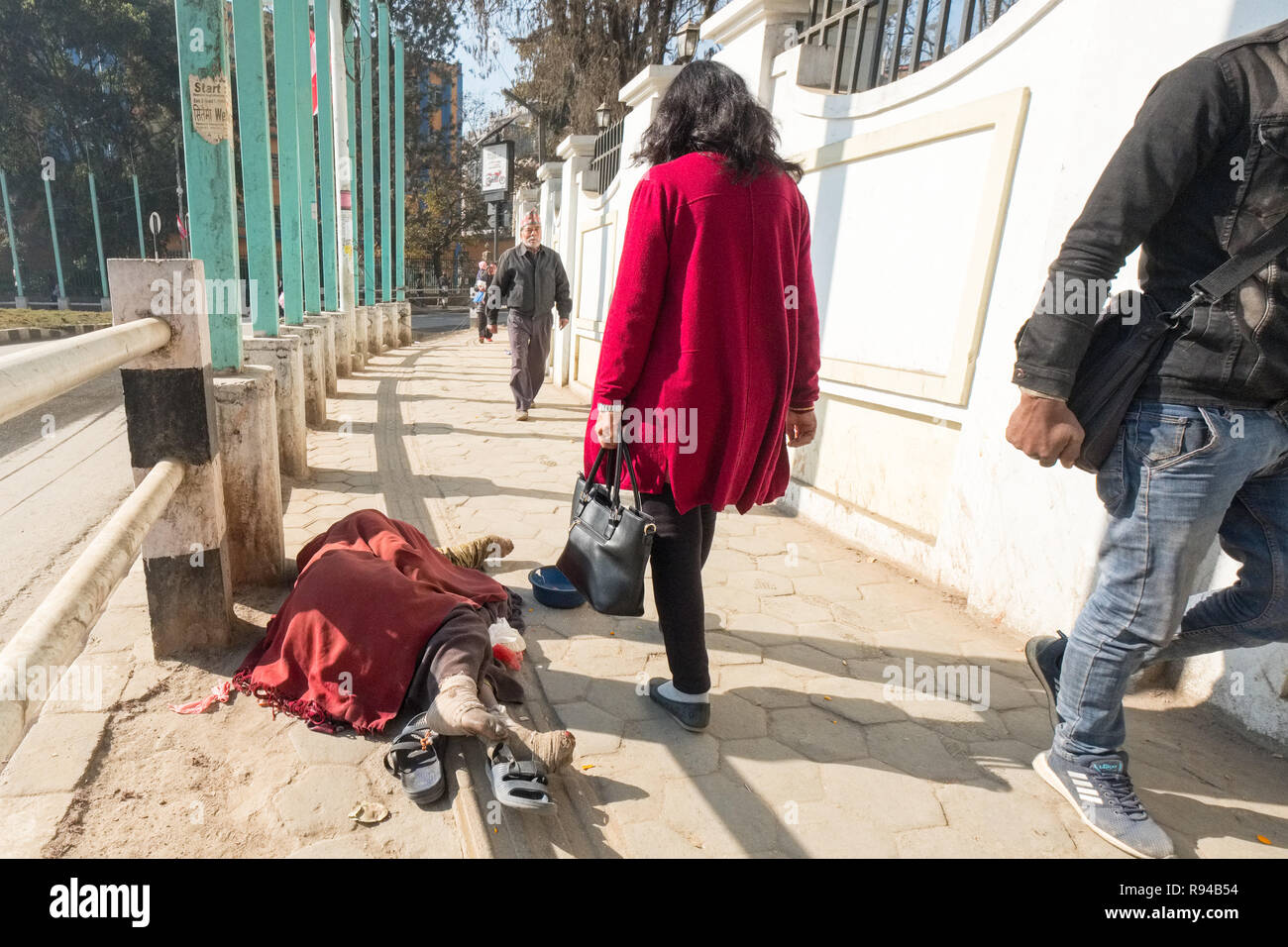 Pedestrians on a Kathmandu street walk past a prostrate disabled beggar suffering from Leprosy, Nepal, Asia Stock Photo