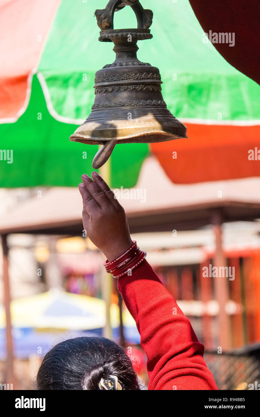 Nepalese woman ringing a bell at a temple in Kathmandu, Nepal Stock Photo