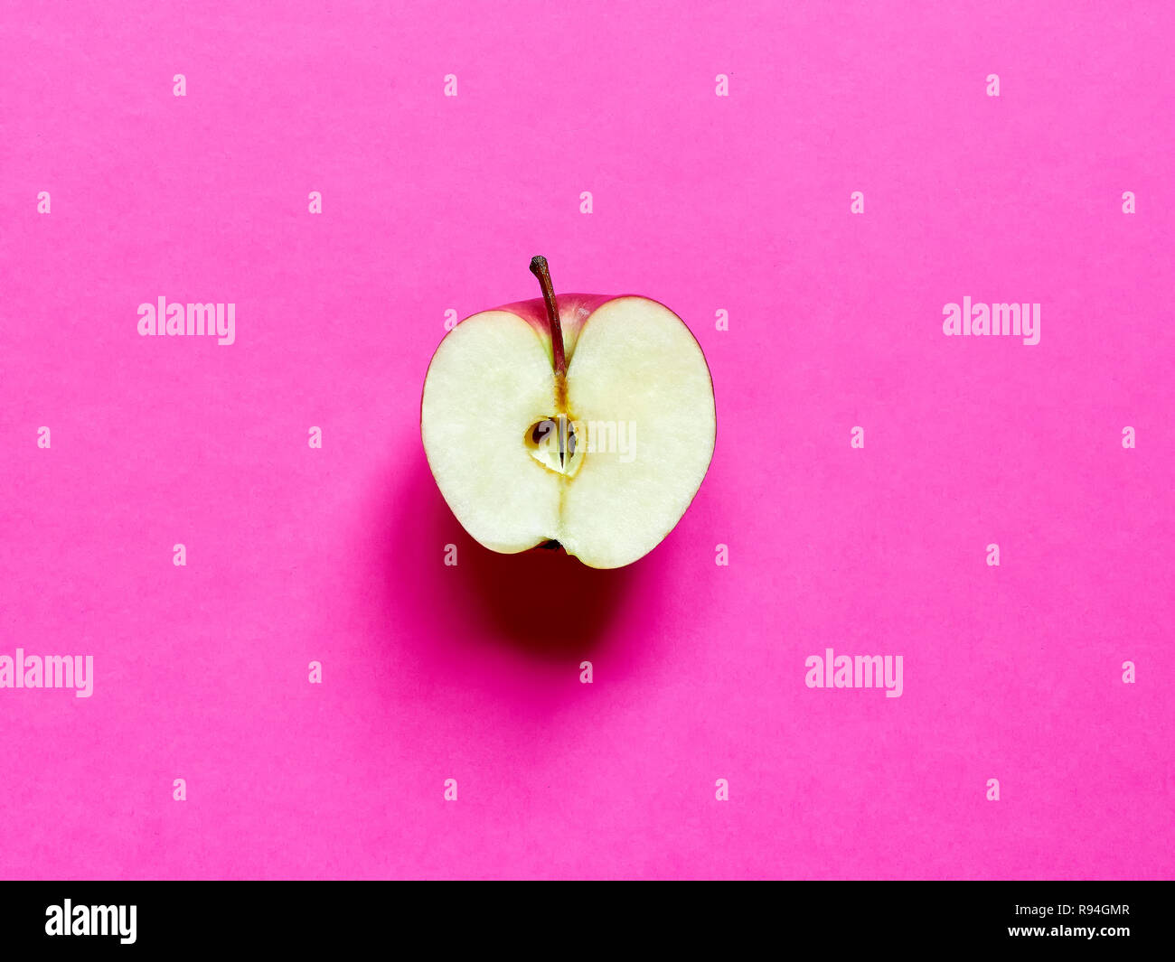 Apple fruit sliced by half isolated in studio over a fucsia pink background Stock Photo