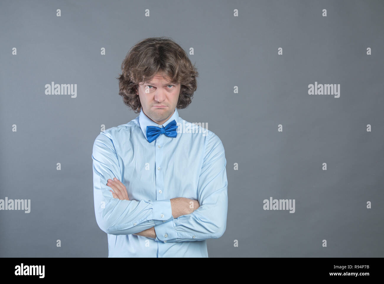 Resentful man with arms folded over gray background in studio shot and offended looked at camera. Angry grumpy guy looking very displeased. Negative h Stock Photo