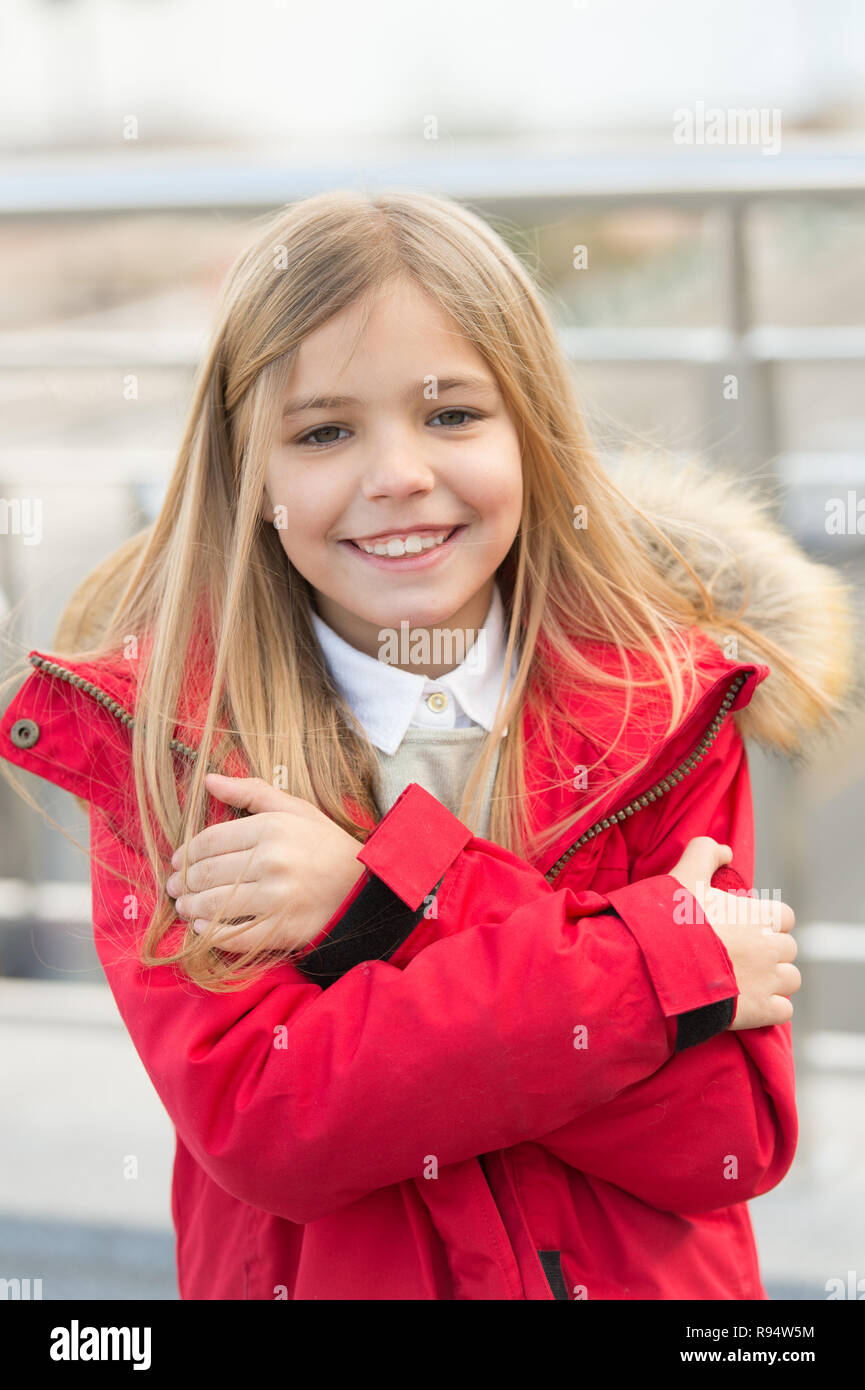 Kid smiling girl wear coat jacket with fur on hood but feels cold. Cold weather concept. She is freezing. Baby hug herself because of cold weather. Kid try to warm up outdoor